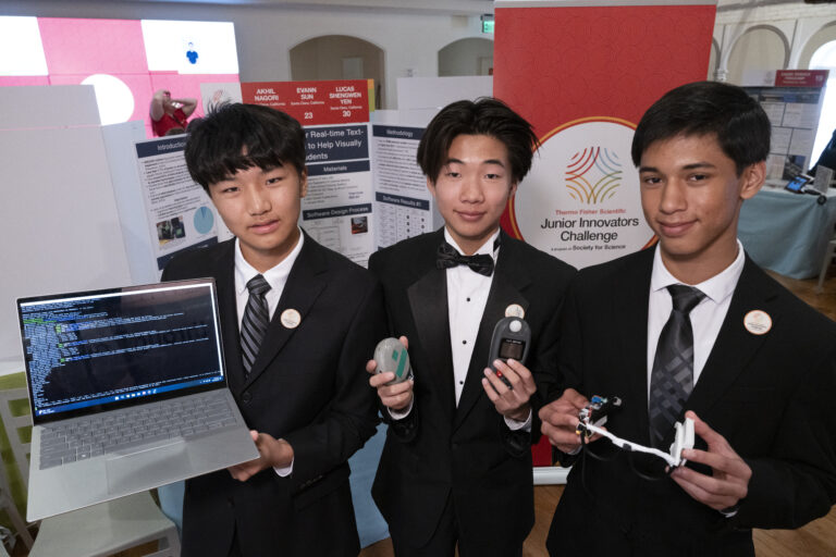 Teammates Evann Sun holding a laptop, Lucas Yen, and Akhil Nagori holding their protoype at the Junior Innovators Challenge.