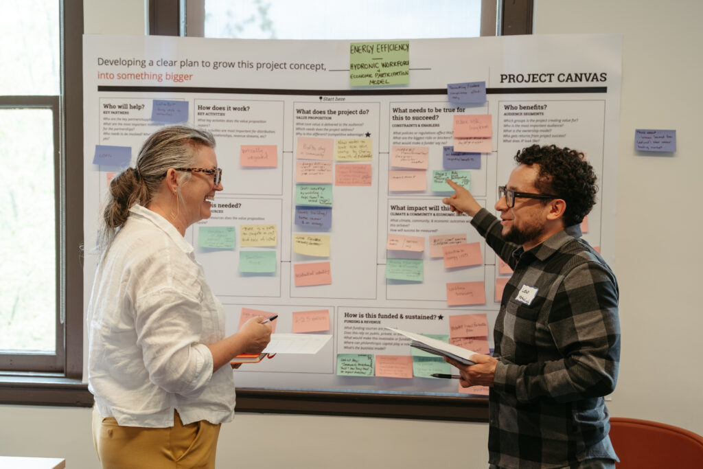 Two people in conversation in front of a project board.