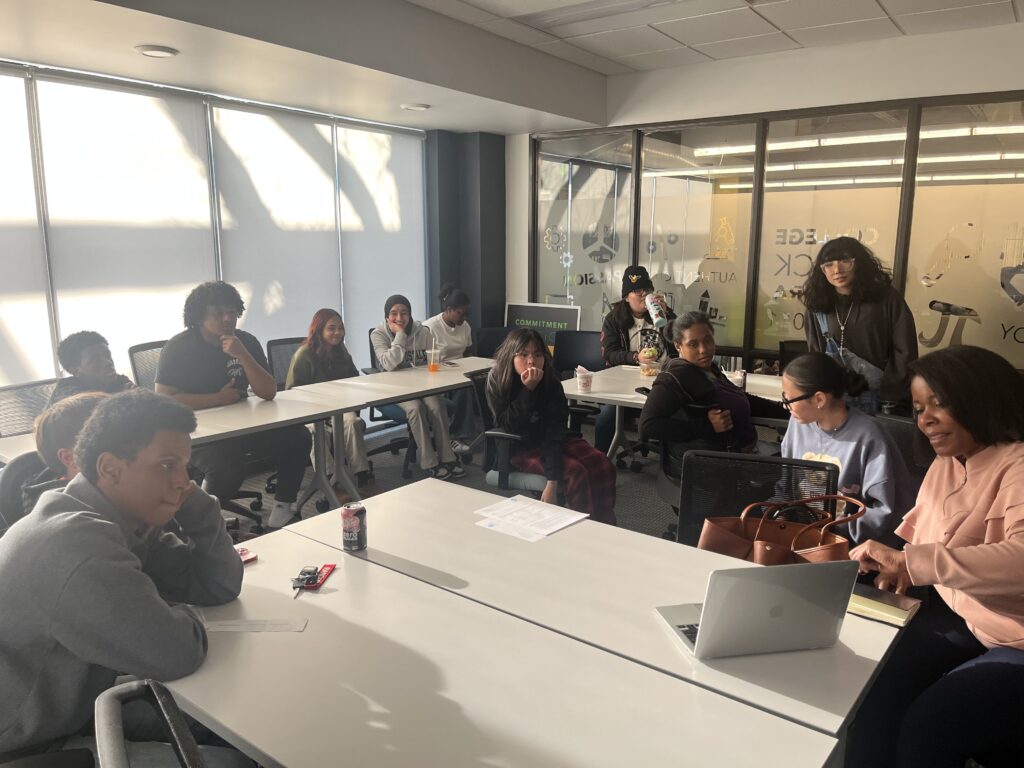 Students and a woman sit around a white table in a classroom.