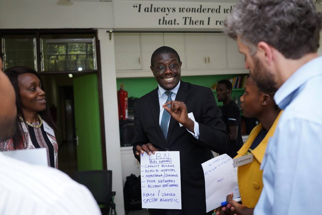 Five participants connect and network with like-minded peers during Peer Powered Workshop, Nairobi. A man wearing a suit in the center of the photo holds up a list.