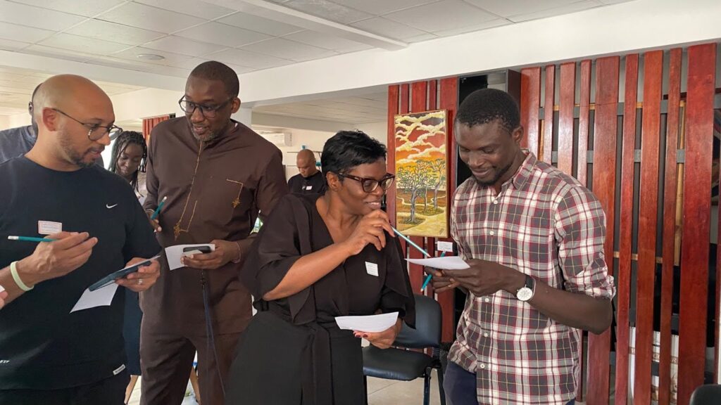 Four participants dive into a Human Bingo icebreaker activity during Pollinate Pulse, Dakar. The individuals look down at their bingo cards.