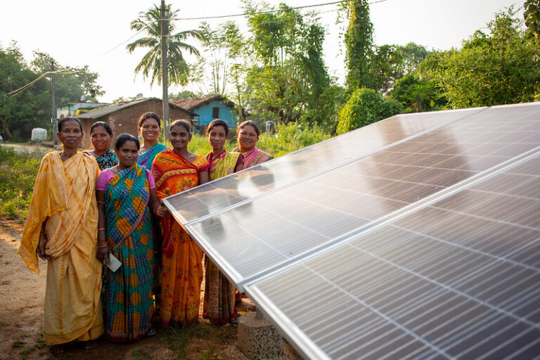 A group of woman stand next to a solar panel.